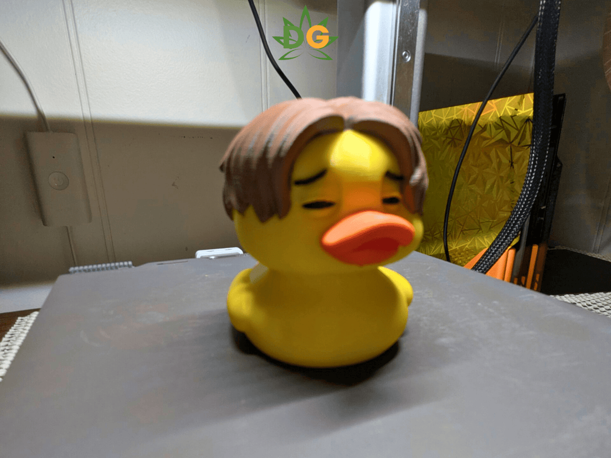 A yellow rubber duck wearing a brown center-parted wig as an alternative metal-style collectible display piece.